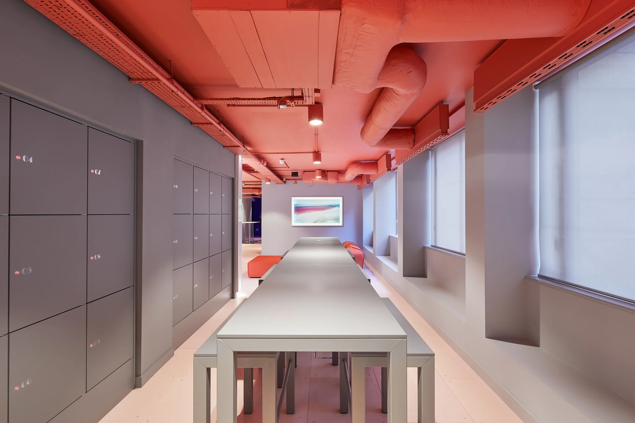 A modern workspace with grey lockers, grey high table and pink ceiling