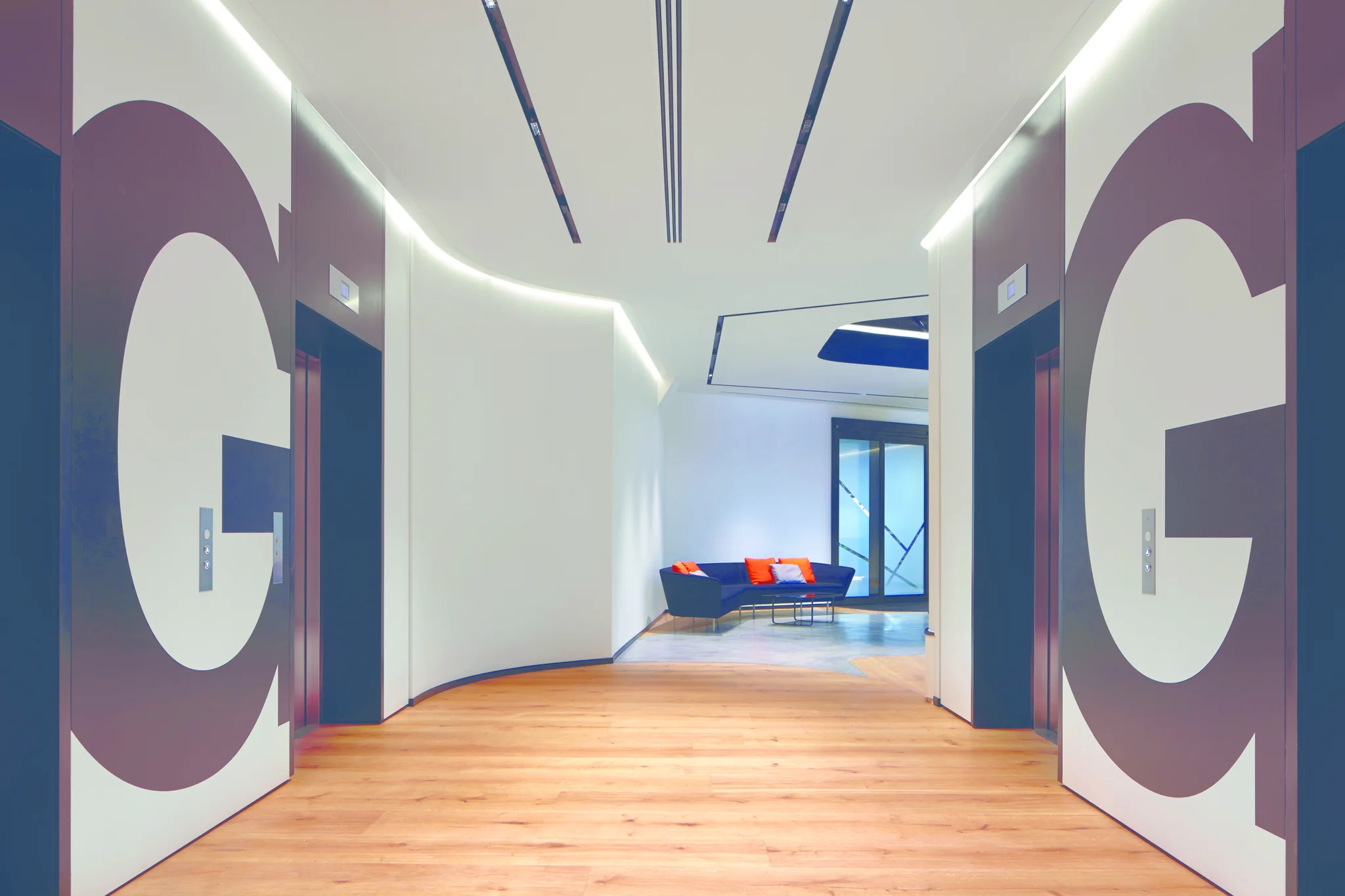 Ground floor lift lobby with giant G wall signage in foreground & sofa with bright orange cushions