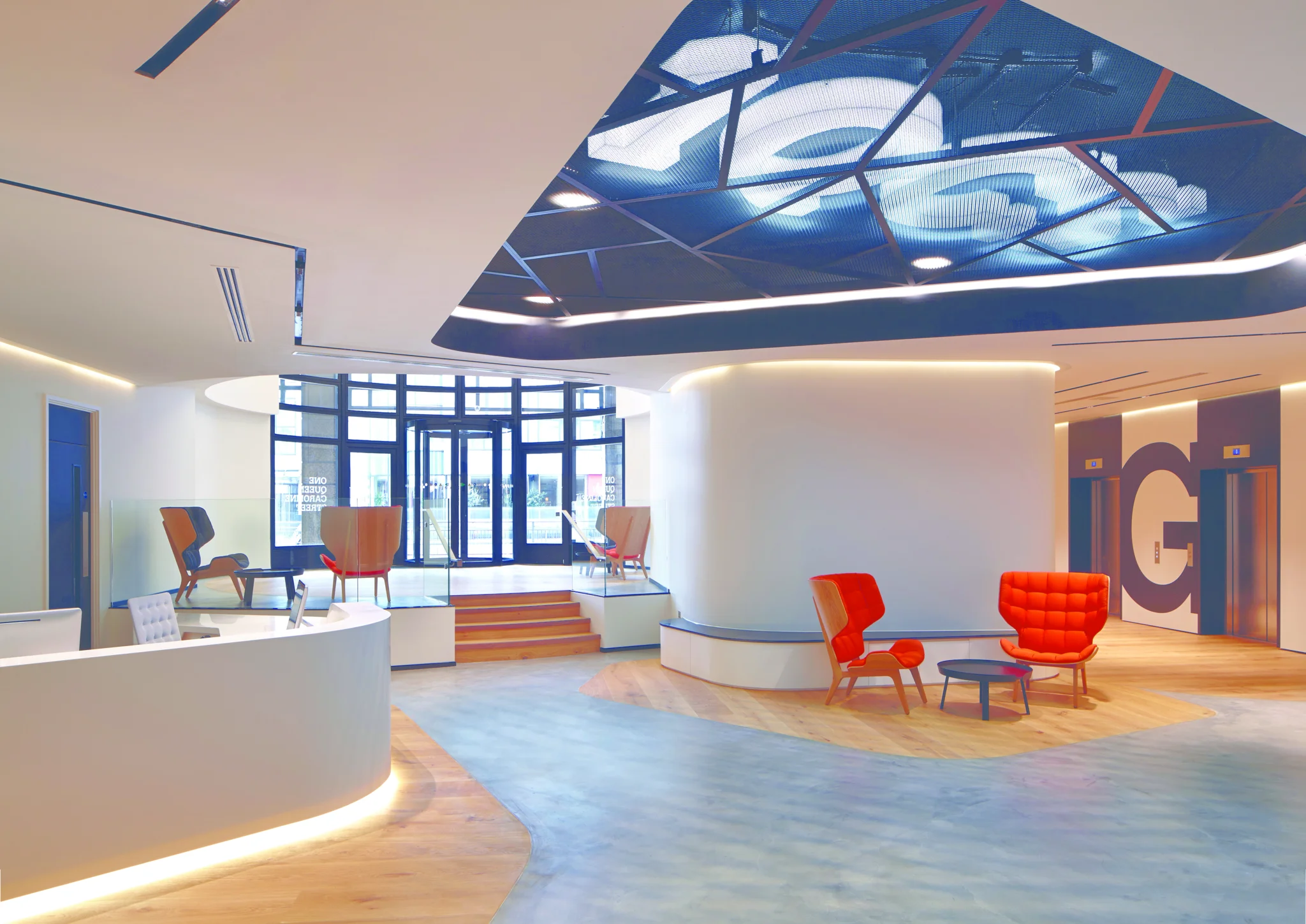 Reception area with reception desk, orange chairs, white walls and 1QS white lighting signage in ceiling