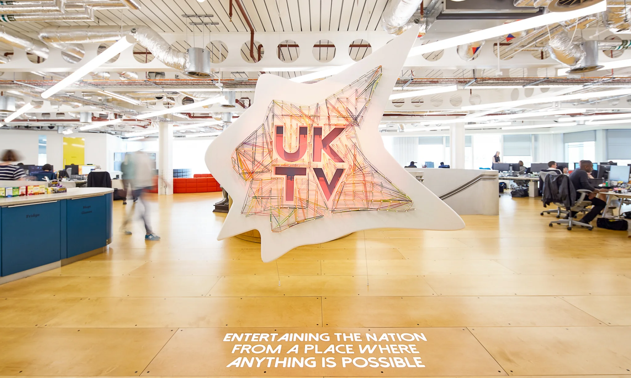 brightly coloured UKTV sign hanging from the centre of a busy workspace