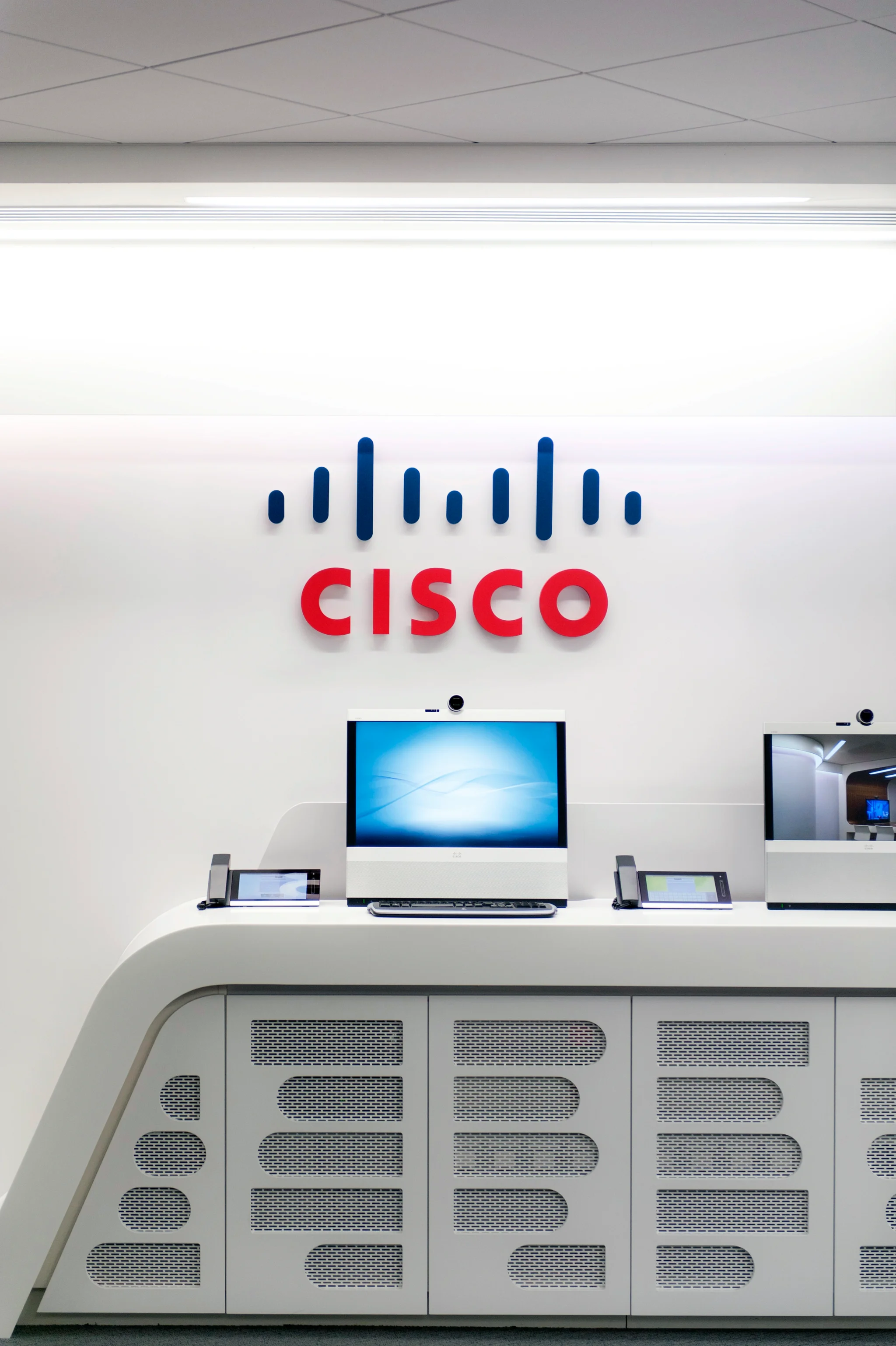 cisco red & blue logo on a white wall above a shelf with blue computer screen