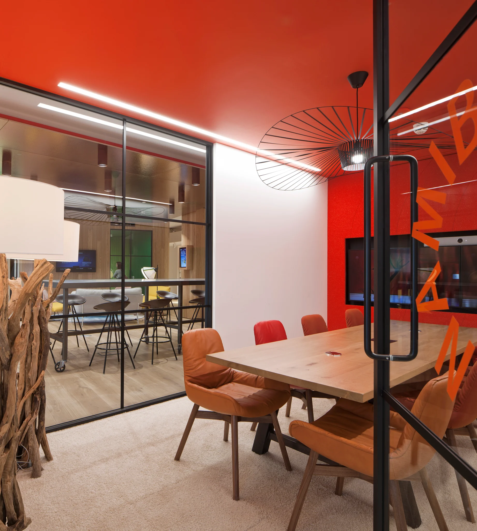 红色会议室的一个明亮的镜头，尽头是电视屏幕，有一张木桌和棕色的皮椅，还有白色灯罩的笨重的木灯。