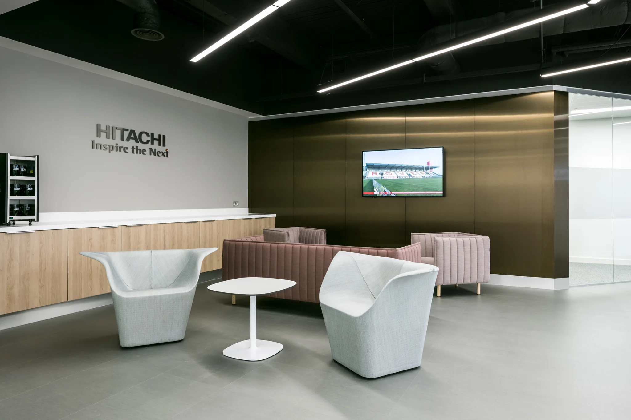 Hitachi reception with a minimal style of grey gloss floors, metallic bronze wall, architectural-style chairs, and pink sofas