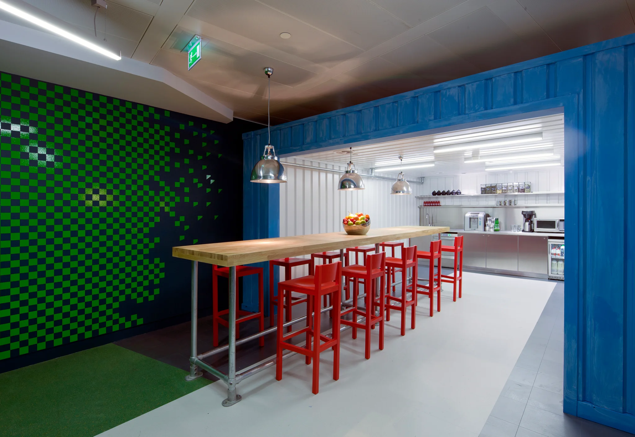 A blue, green & white kitchen space with wooden table & red stools
