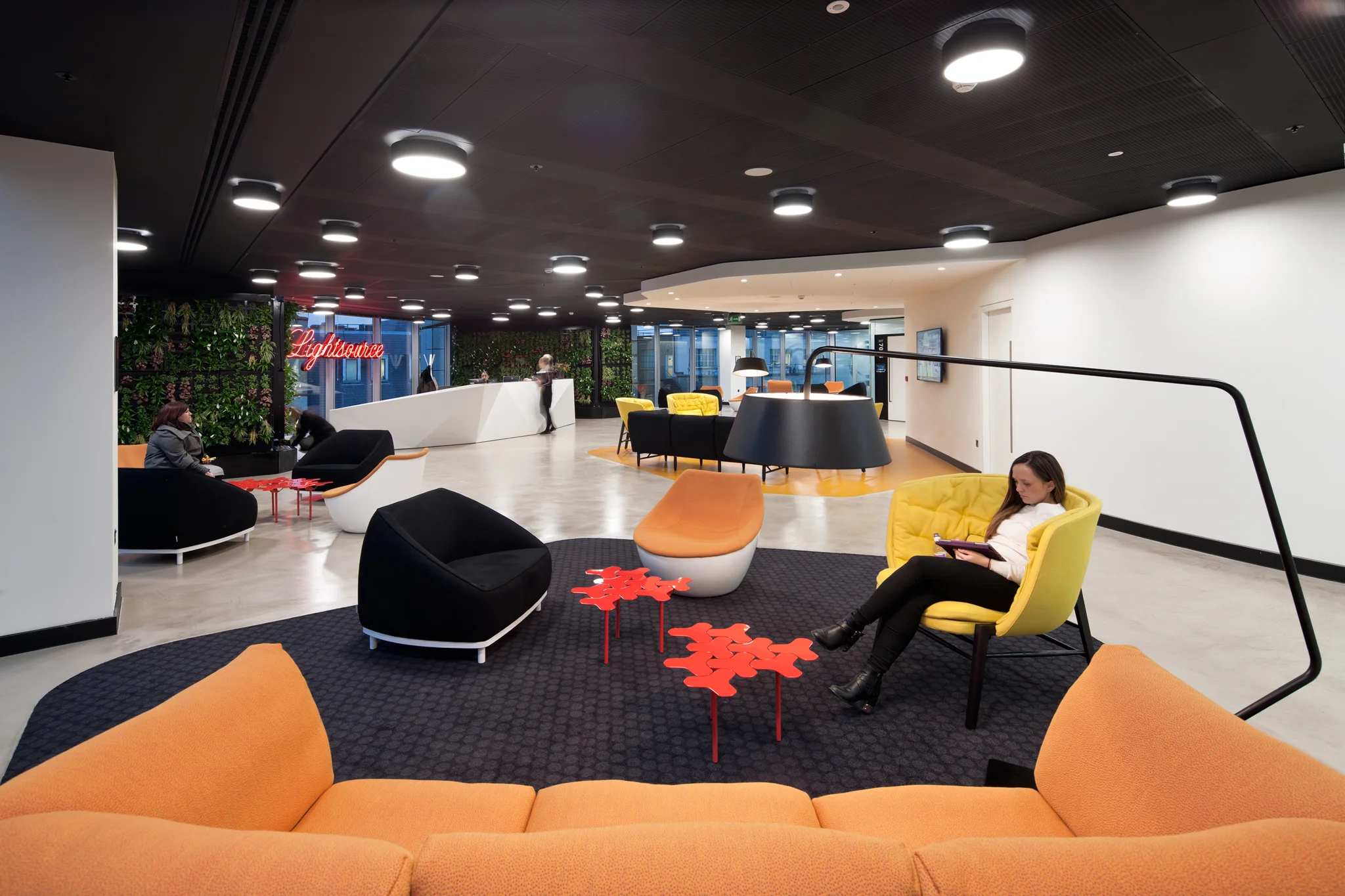 reception area with orange and black breakout seating areas & people using the space. A white reception desk sits in the background
