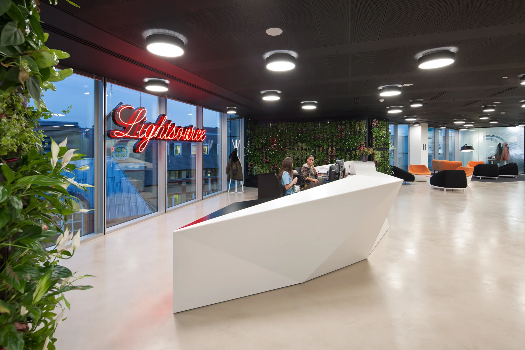 lightsource reception desk with the brand logo in a neon sign behind, flanked by two green living walls