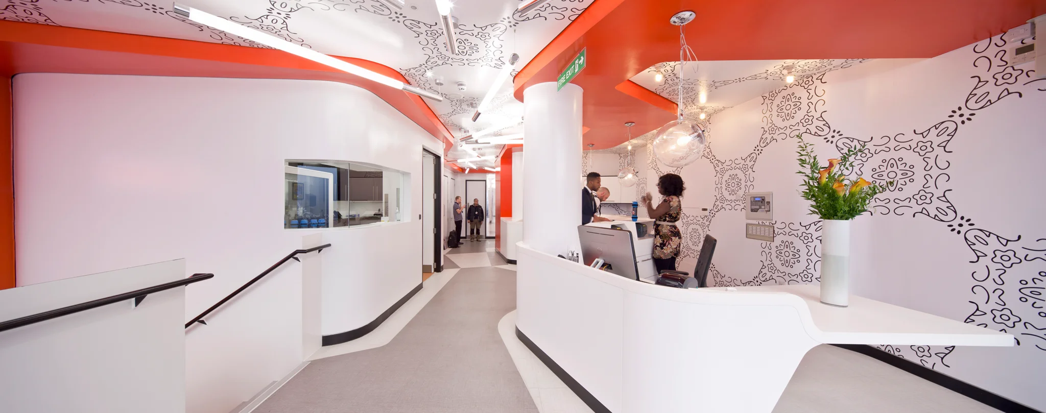 woman standing behind a white reception desk - set against coral coloured walls
