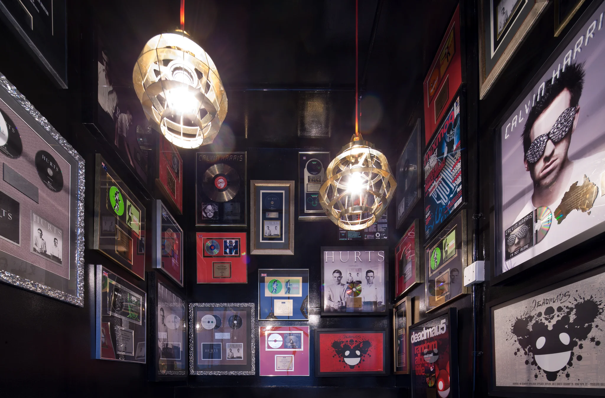 A black stairwell with album artwork & awards covering the walls. Two pendant lights hang down in the space