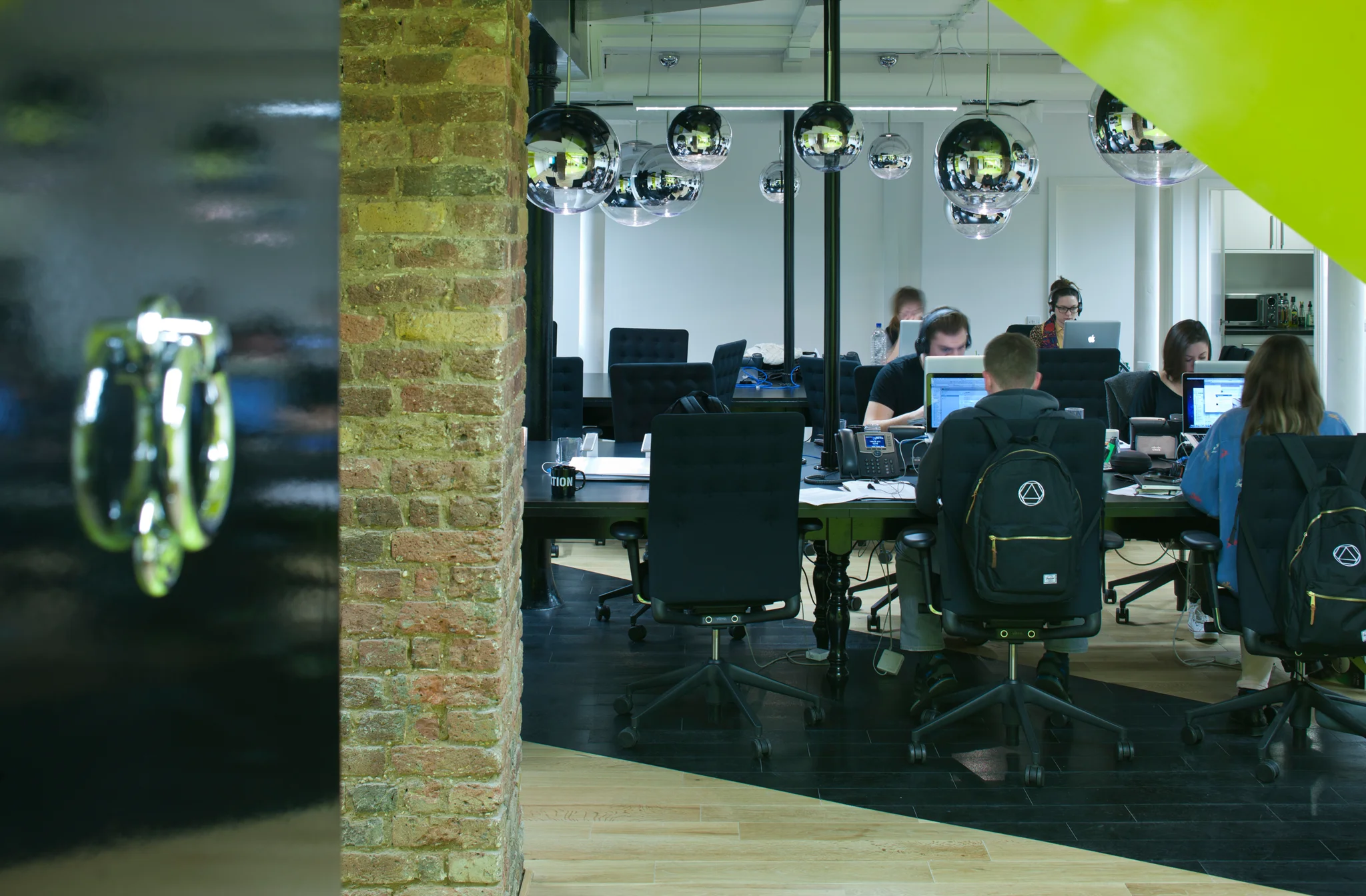 Workspace with exposed brickwork, black glossy surfaces & people working at computers