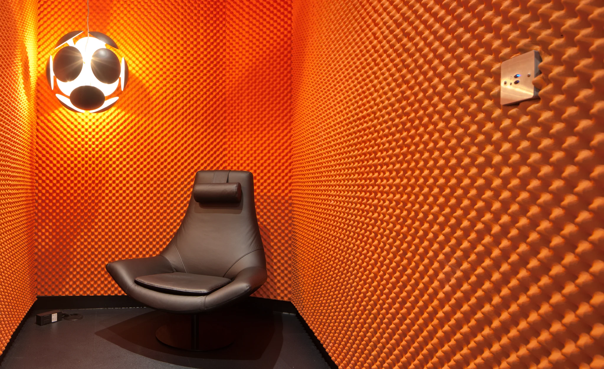 Bright orange acoustic bobbled pod with suspended light & brown leather armchair
