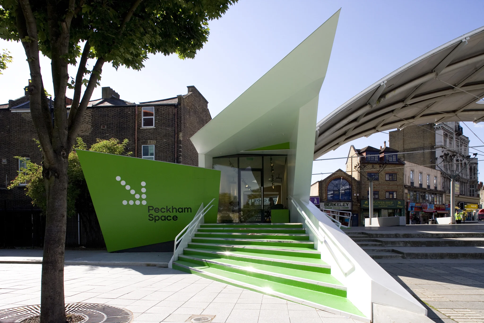 wide angled exterior shot straight on of the green entrance to Peckham space with a white arrow pointing towards the door. Trees & the sky frame the shot