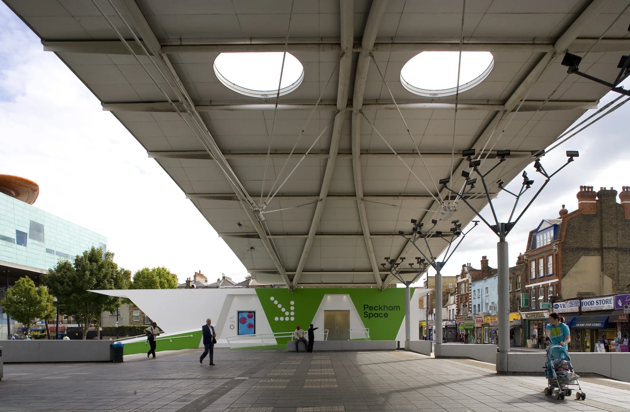 A side view of Peckham Space with white metal canopy structure overhead joining two buildings