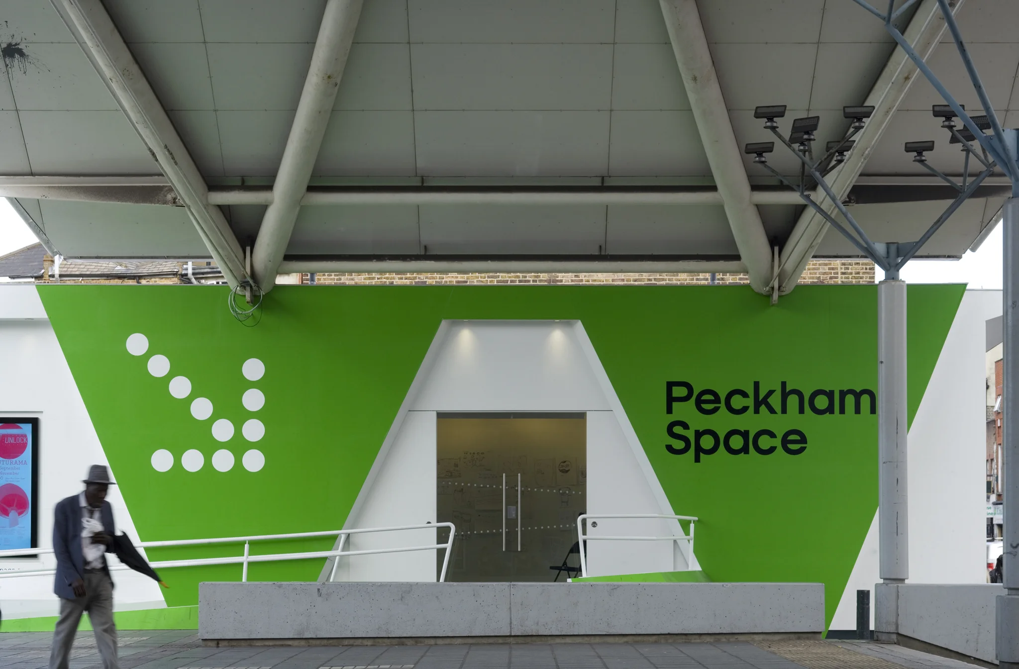 Side view of the side entrance to Peckham Space. Green walls flank the entrance doors below the metal canopy overhead