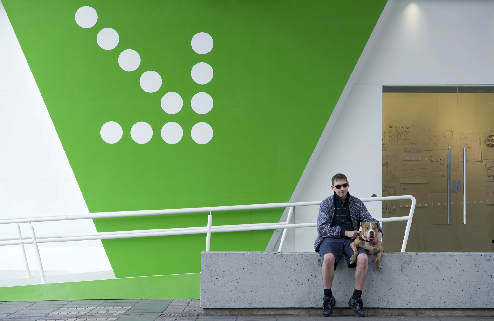 A man sits with his dog on the top of the wall of the side of Peckham Space that leads to the entrance.