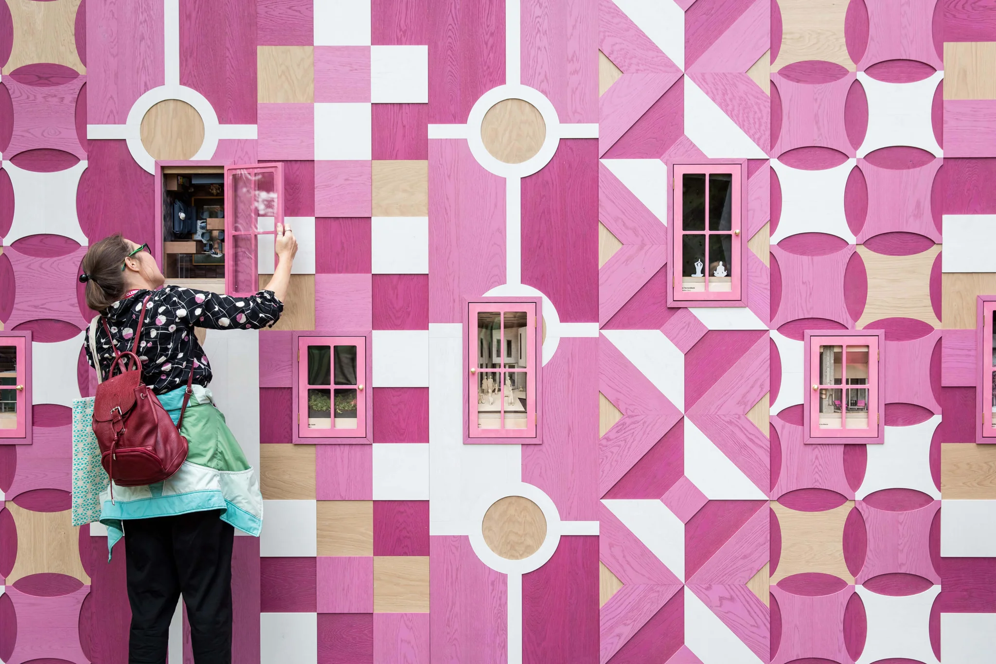 girl stood in front of a pink patterned wall looking into the hidden holes within it