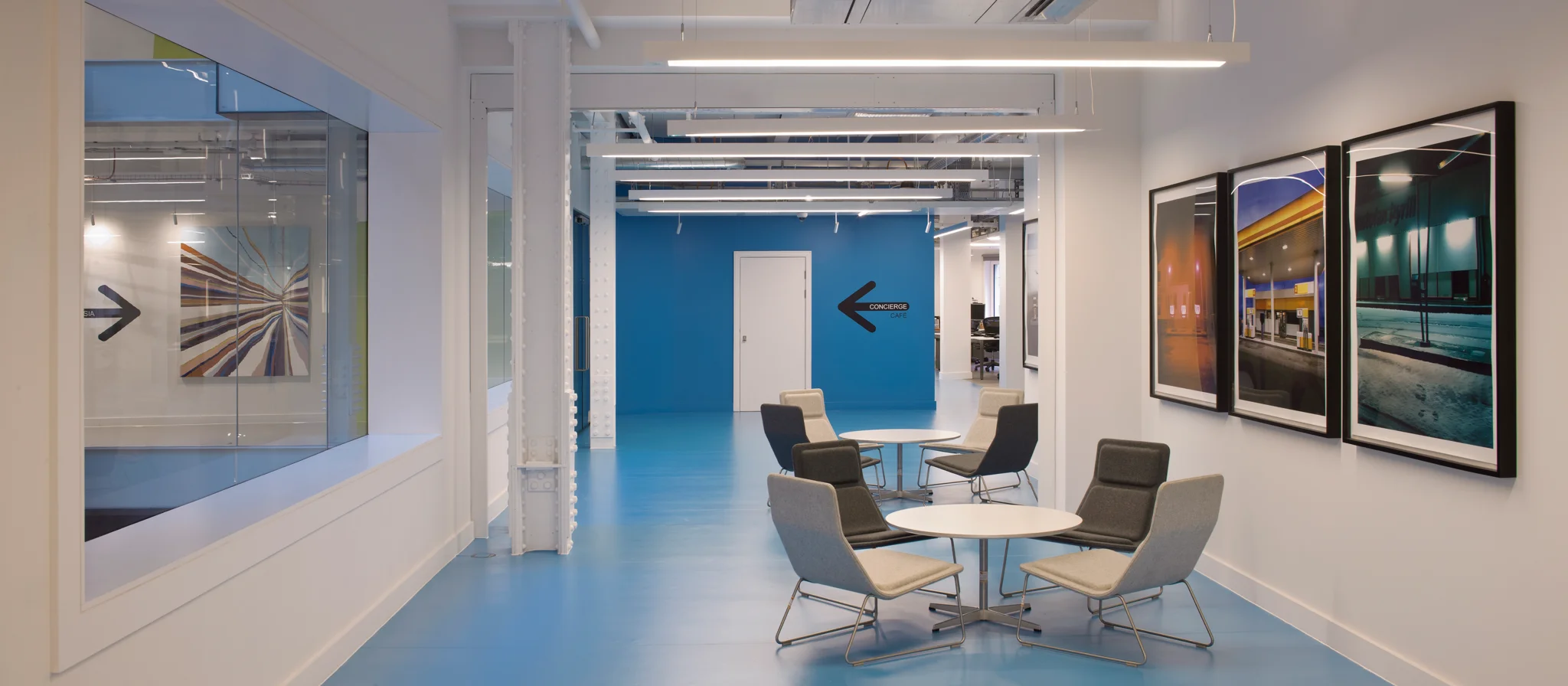 A large corridor with chairs, artwork on the walls and a vivid blue back wall with a black arrow signalling the way to walk