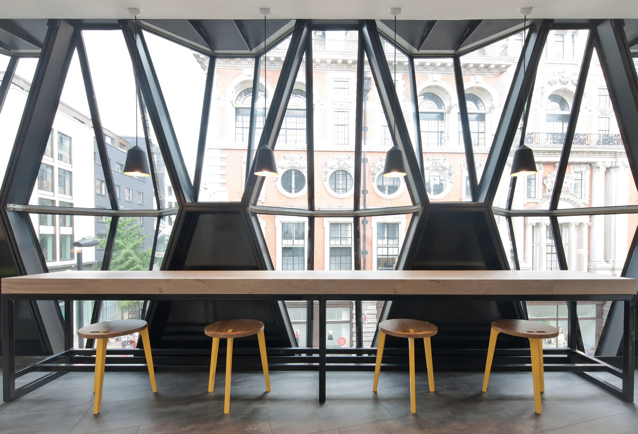 A work bench and stools against glass windows that look out on to Oxford street