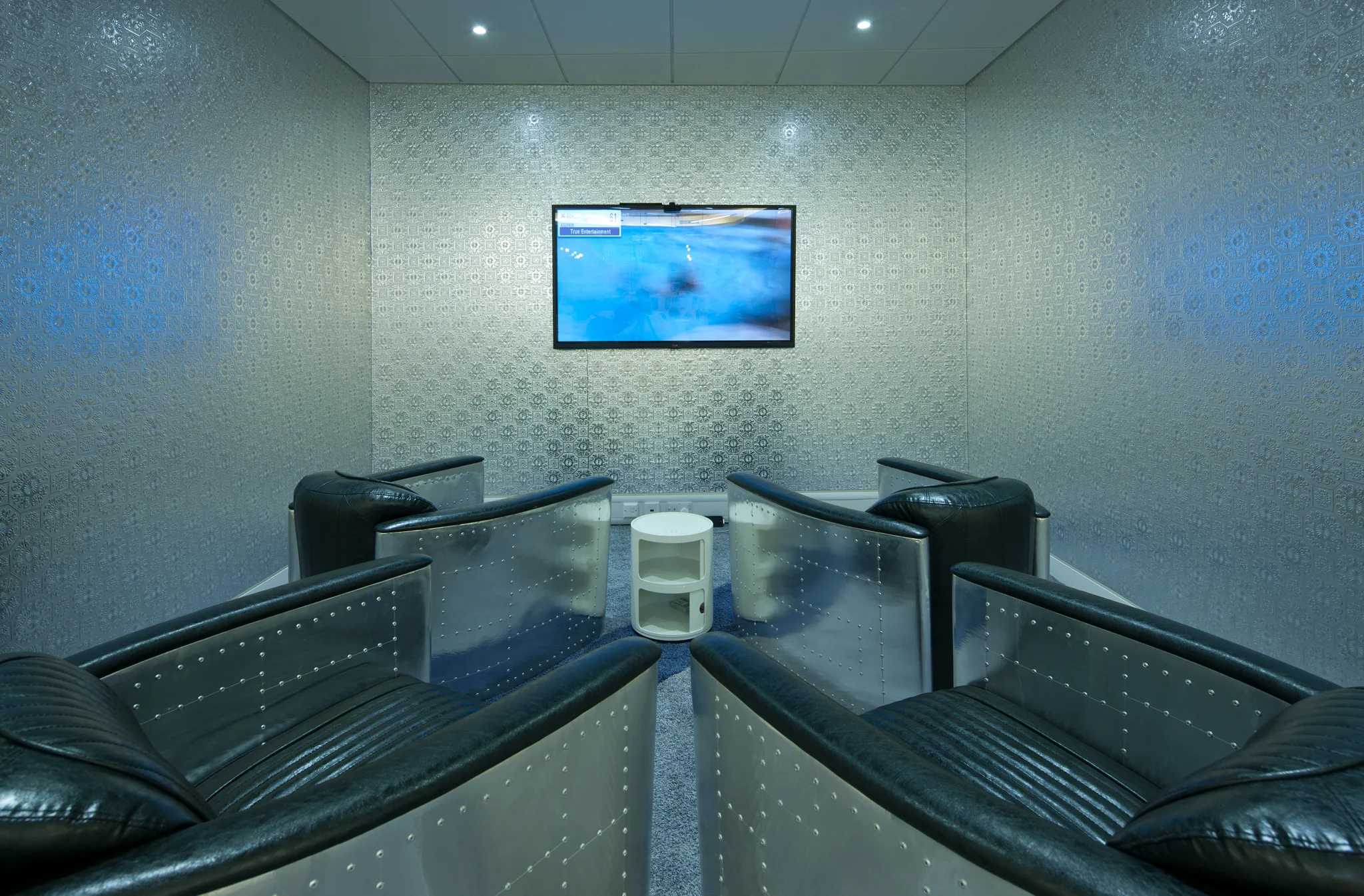 a cinema room with metal punctuated walls, low leather and metal backed chairs and a screen at the end of the room