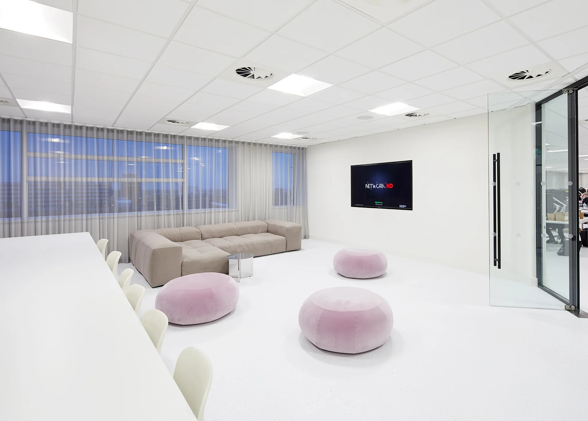 Meeting room with light grey low sofa, white desks, chairs and pink velvet poufs