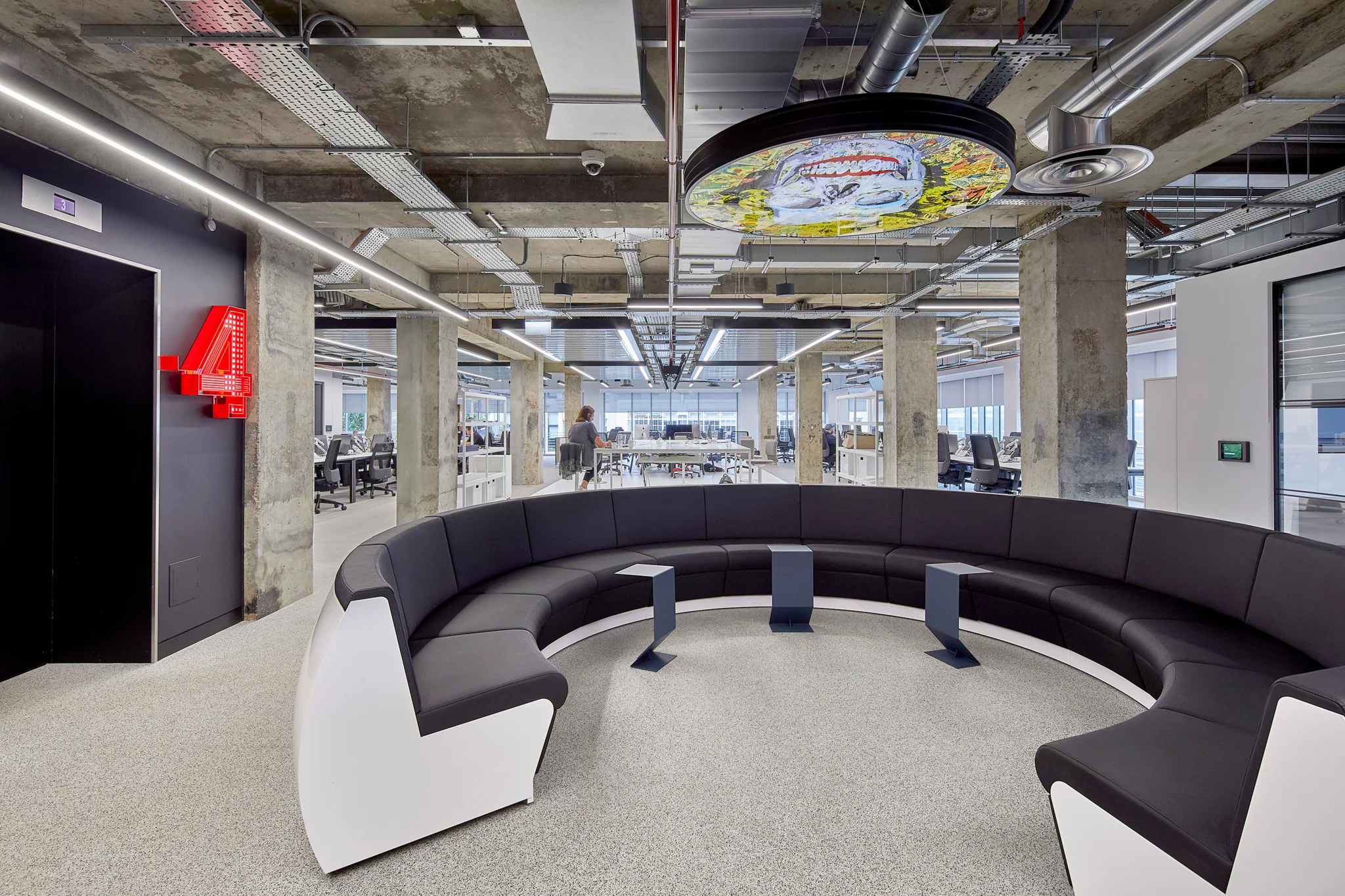 前景是一个巨大的黑白圆形沙发,背景是在工作站工作的人。