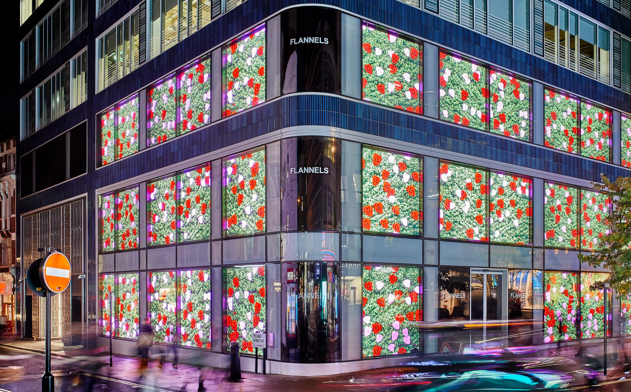 一座玻璃建筑的一角的夜景,下面的窗户有鲜花艺术品,角落的窗户有Flannels文字