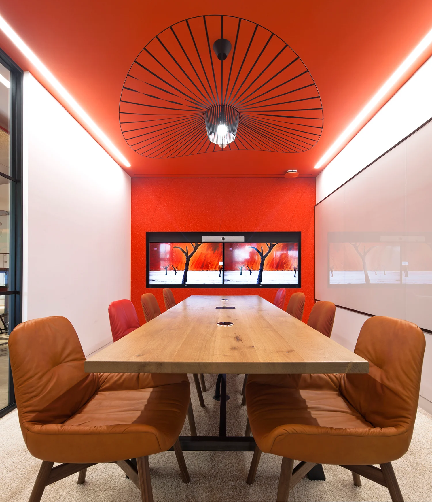 A bright red meeting room with a TV screen at the end & with a wooden table & brown leather chairs