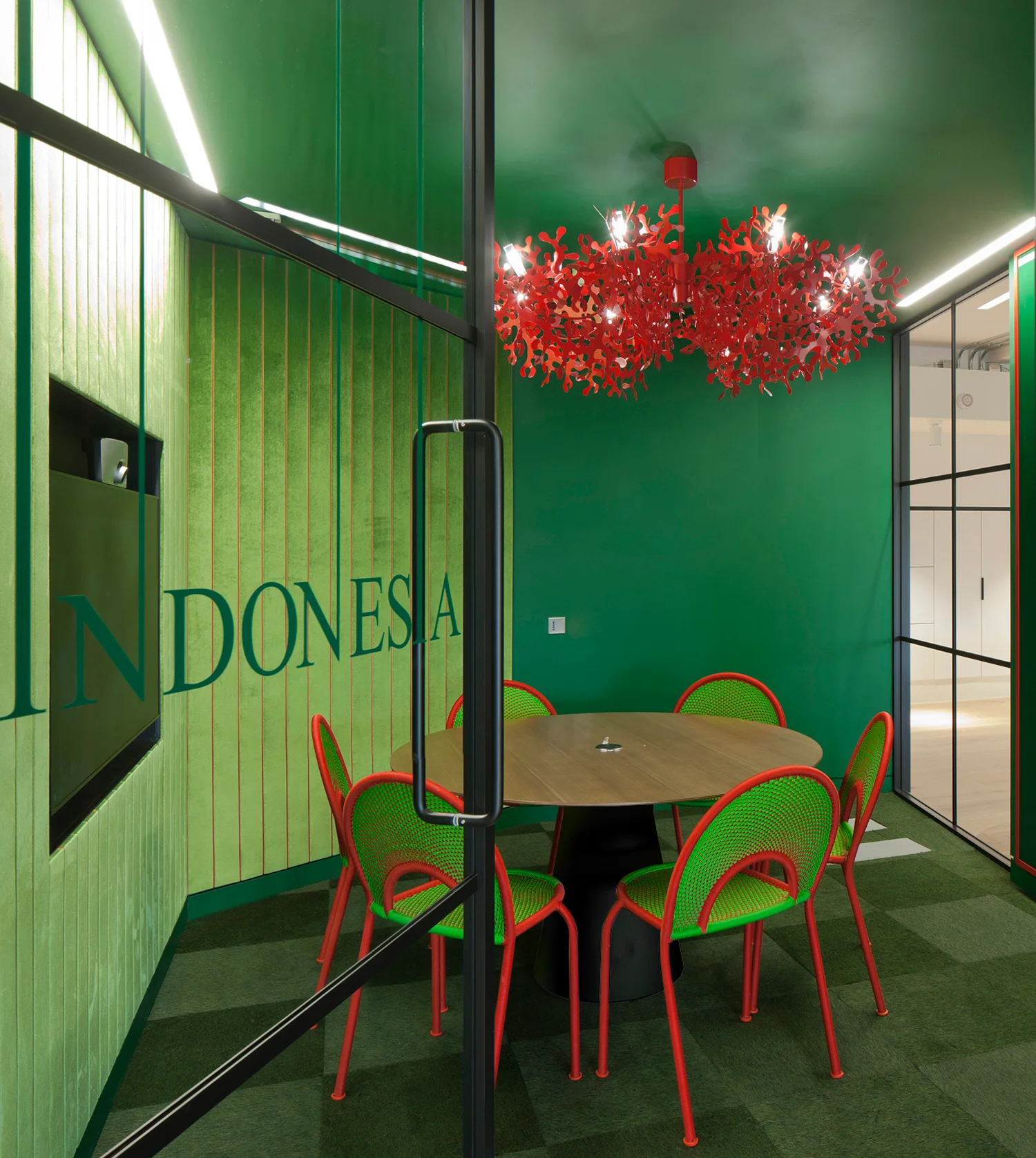 Bright green meeting room with bright red coral-like suspended light over a wooden table & green & pink chairs