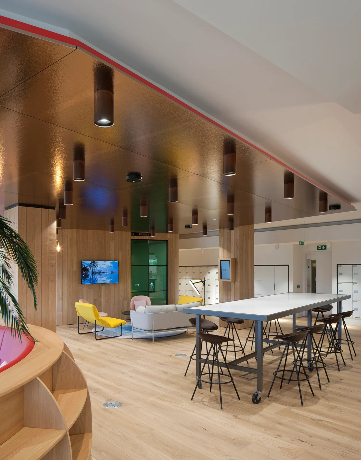 Gold ceiling, wooden floor & walls with bright yellow, light pink chairs and light grey sofa in an arrangement behind a high table and chairs