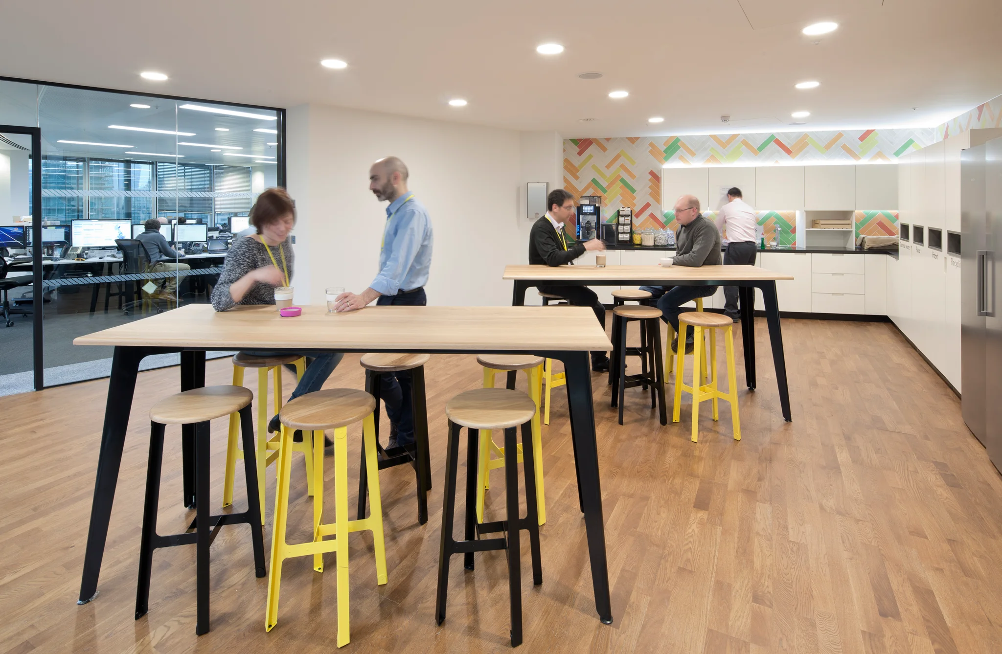 A kitchen area with high stools and tables and people using the space