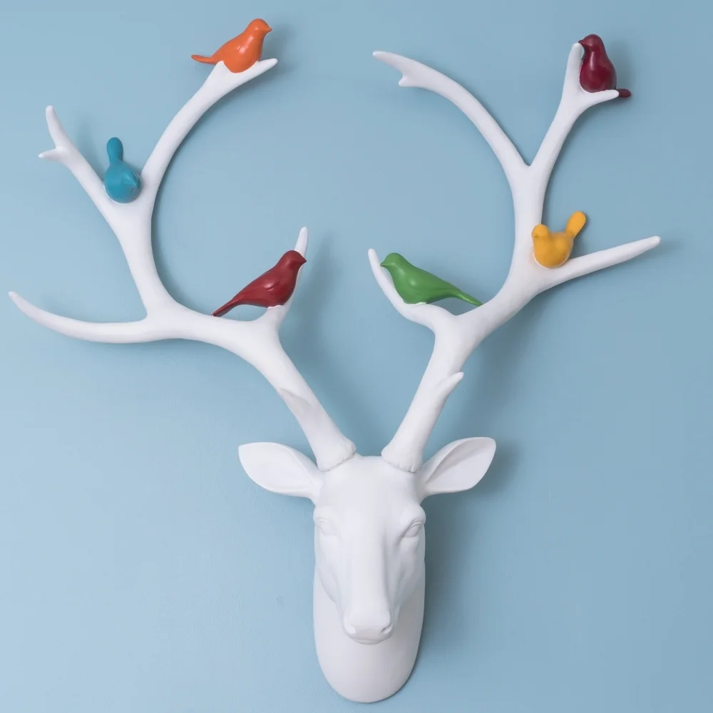 white stag head with bright coloured birds in the antlers on a blue wall