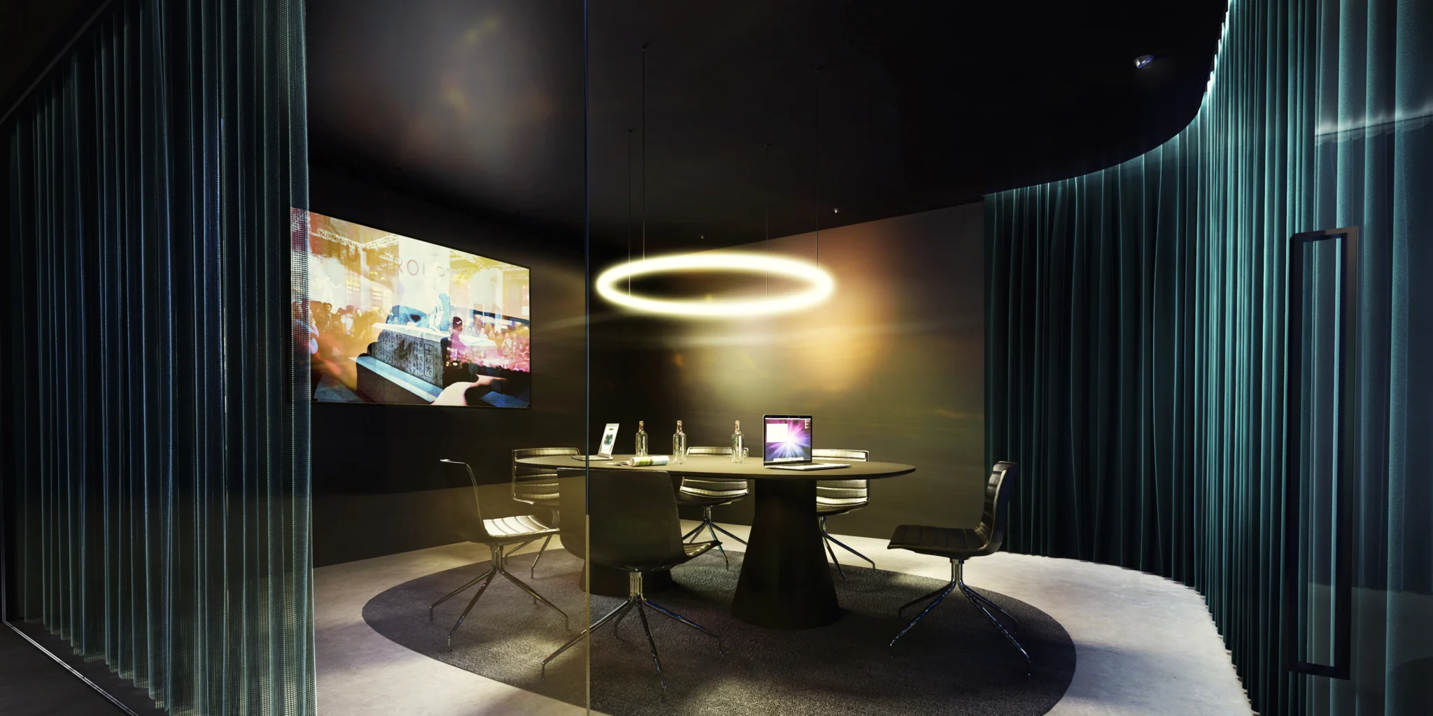 A meeting room with suspended circular light and black table & chairs in front of a tv screen